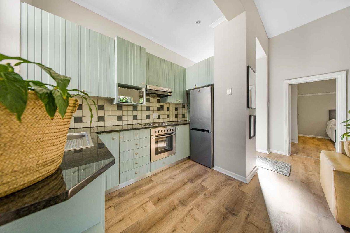 A functional kitchen featuring light green cabinetry, granite countertops, a tiled backsplash, and integrated appliances, with laminate flooring throughout.