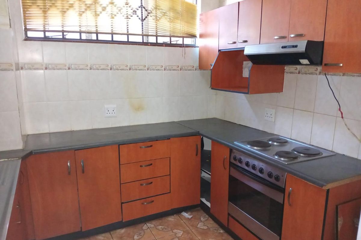 A dated kitchen featuring laminate cabinetry, built-in oven, electric hob, and extractor fan, requiring cosmetic updates and repairs to finishes.