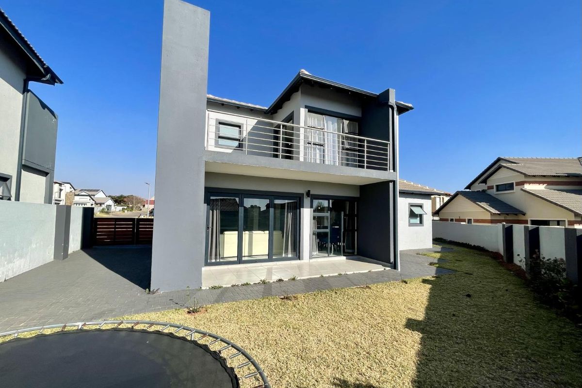 Rear view of a modern two-story house featuring a paved patio, a balcony with metal railings, and large sliding glass doors.
