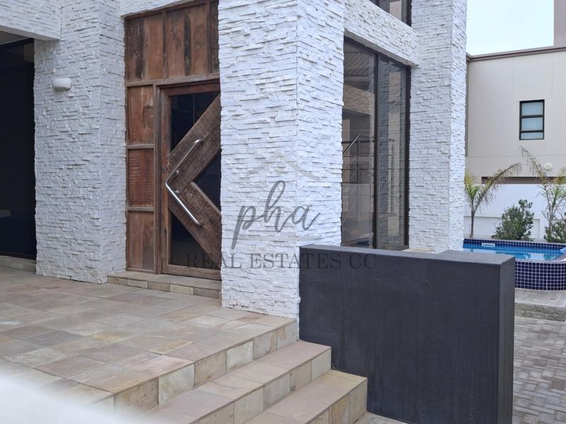 Modern entrance featuring a striking timber pivot door, stacked stone facade, tiled steps, and a private courtyard with a swimming pool.