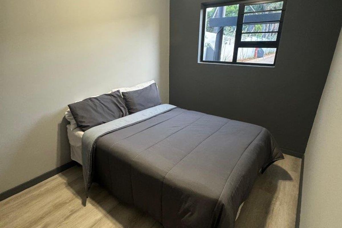 A compact bedroom featuring modern laminate flooring, neutral wall tones, and an aluminium-framed window.