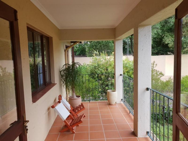 A covered balcony featuring terracotta floor tiles, wrought iron railings, and direct access to the garden area.