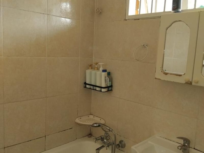 A compact bathroom featuring a bathtub, wall-mounted basin with vanity storage, and tiled walls, requiring some cosmetic updates to improve its overall condition.