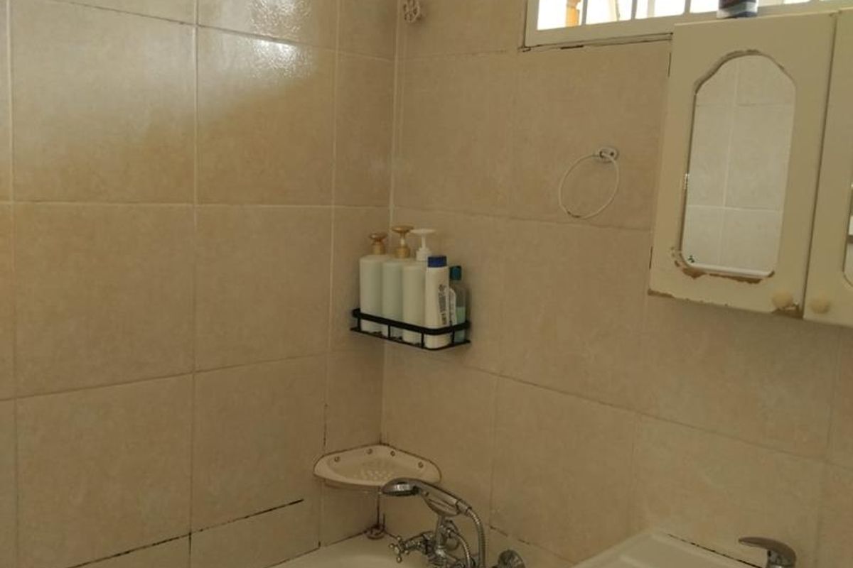 A compact bathroom featuring a bathtub, wall-mounted basin with vanity storage, and tiled walls, requiring some cosmetic updates to improve its overall condition.