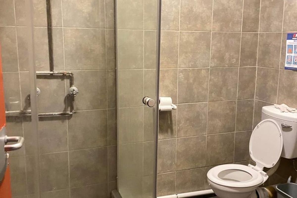 A functional bathroom featuring a shower enclosure with exposed plumbing, a standard toilet, and tiled wall and floor finishes.