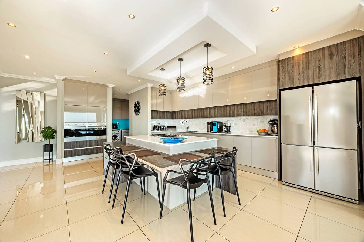 Modern open-plan kitchen featuring high-gloss cabinetry, a central island with integrated seating, recessed ceiling lighting, and polished floor tiles.