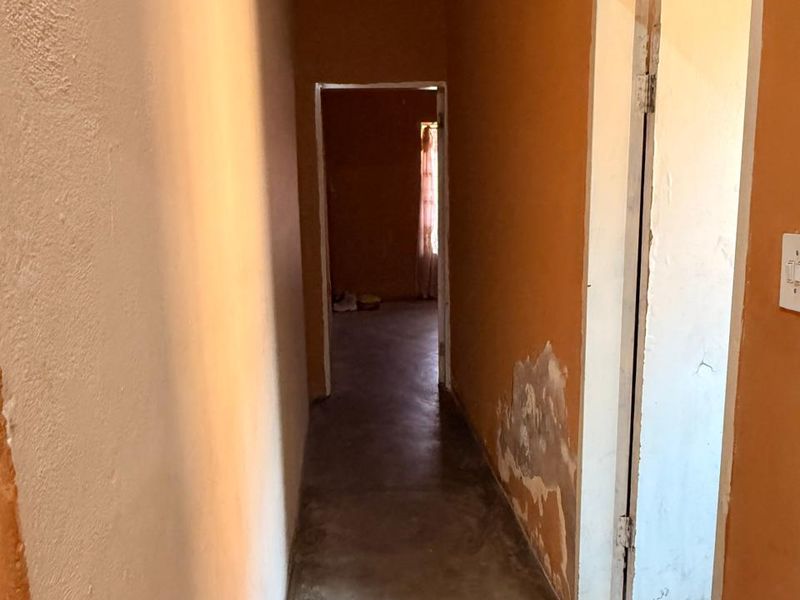A narrow interior hallway featuring orange painted walls with visible surface damage and peeling paint, leading to an adjacent room.