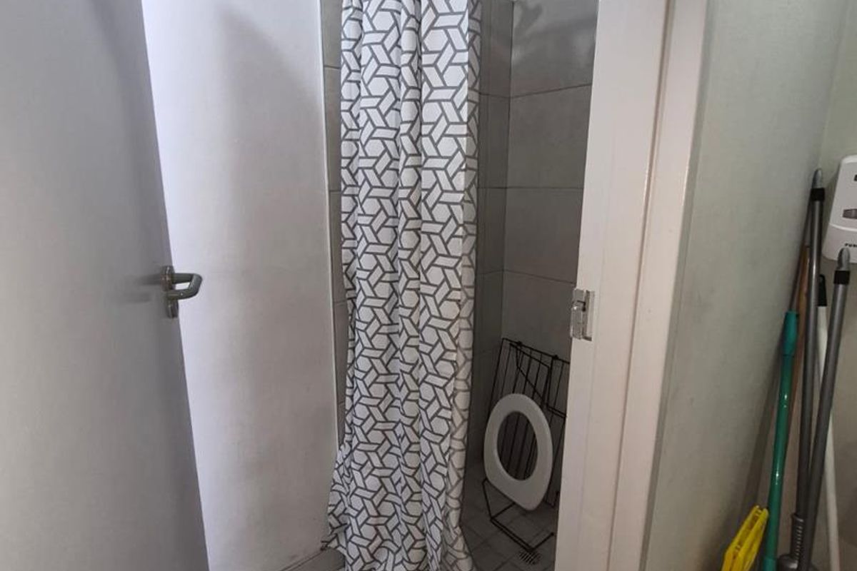 A compact bathroom featuring a tiled shower enclosure with a curtain rail and basic floor tiling.