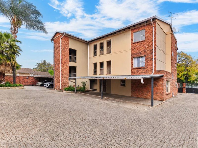 Front exterior view of a multi-story apartment building featuring brick and plaster facade, covered parking area, and paved driveway.