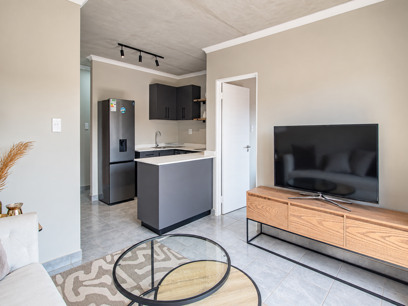 Modern open-plan living area featuring a sleek kitchen with dark cabinetry, stone countertops, tiled flooring, and an exposed concrete ceiling.