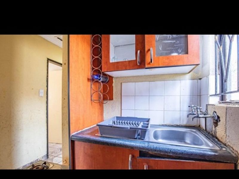 A compact kitchen area featuring built-in cabinetry, a stainless steel sink, and tiled splashback, requiring cosmetic updates to improve its overall condition.