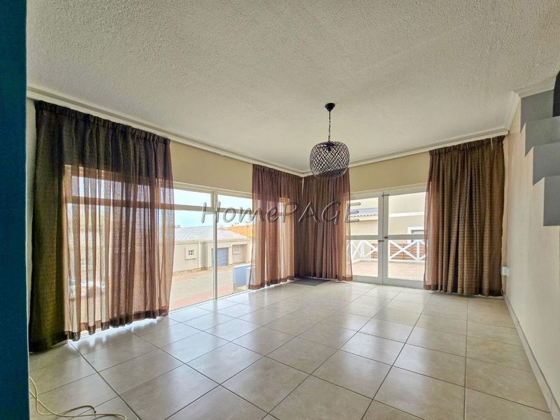 Spacious living area featuring neutral tiled flooring, textured ceilings, and large sliding glass doors providing ample natural light and access to the exterior.