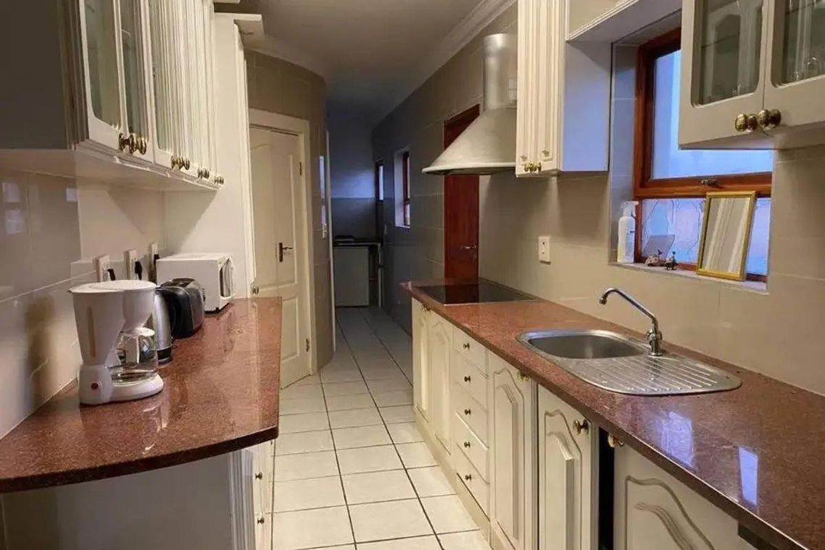 A functional galley-style kitchen featuring granite countertops, white cabinetry, a stainless steel sink, and a built-in extractor fan.