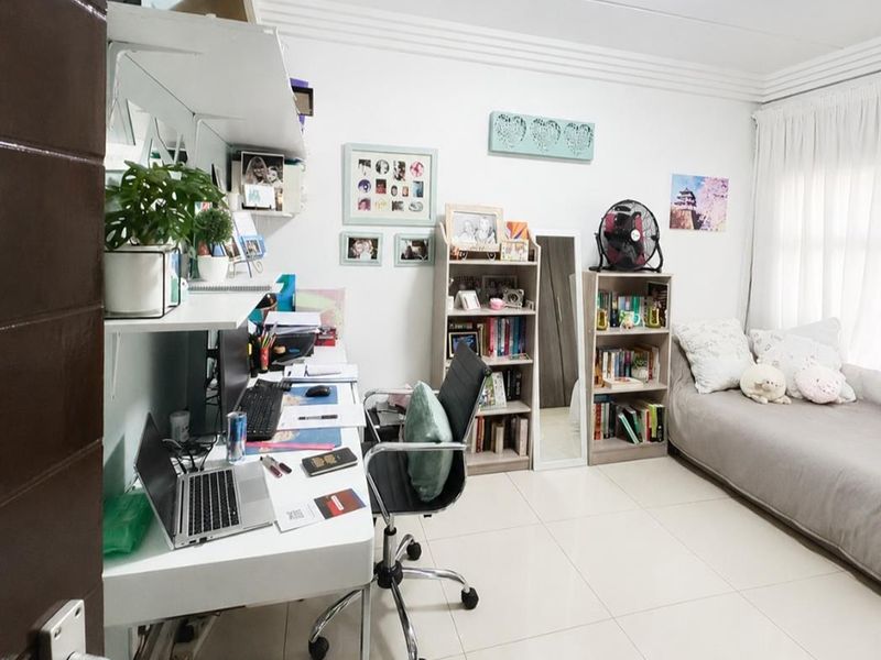 A functional bedroom featuring tiled flooring, built-in shelving, and decorative cornice detailing, currently utilized as a combined sleeping and workspace area.