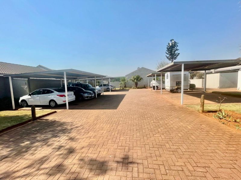 A well-maintained paved driveway area featuring multiple covered carport parking bays within a cluster property complex.