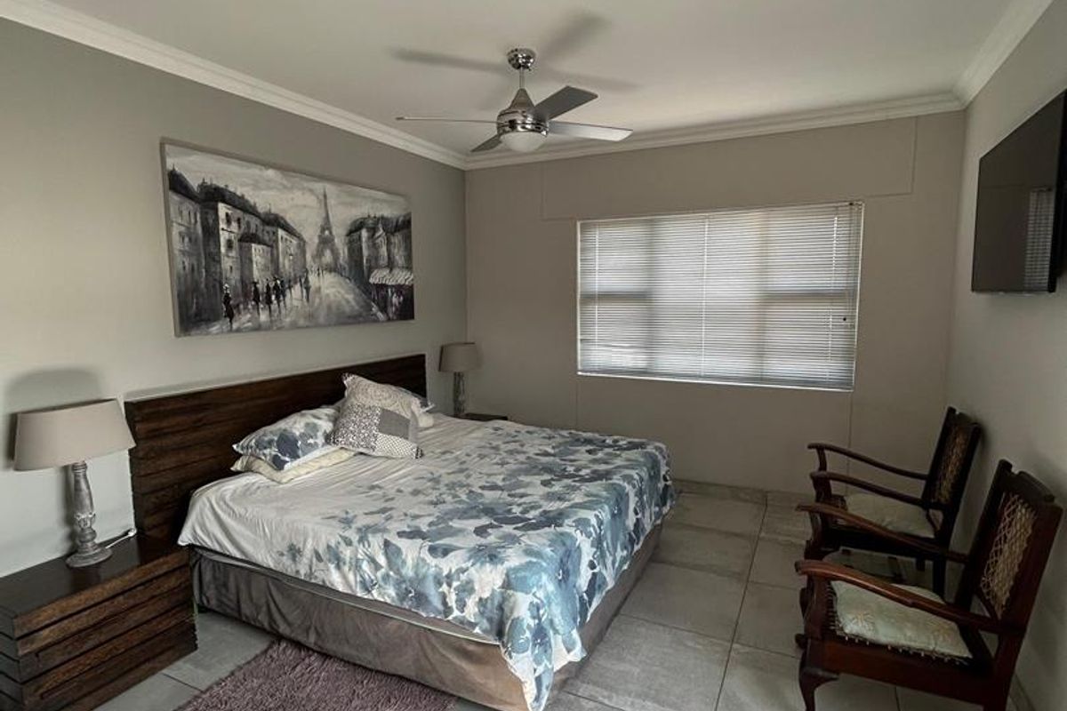 A spacious bedroom featuring neutral tiled flooring, a ceiling fan, and large windows with venetian blinds, offering a clean and well-maintained living space.