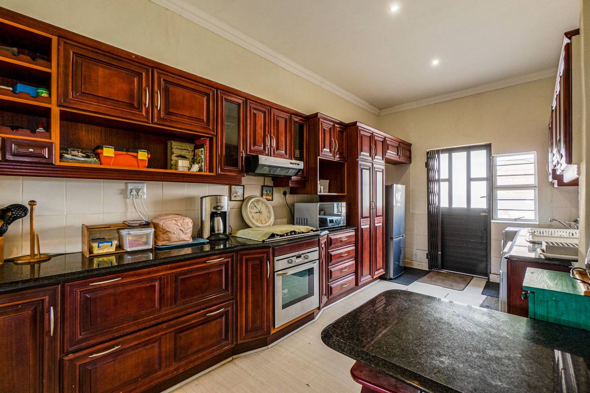 A functional kitchen featuring dark wood cabinetry, granite countertops, built-in oven, extractor fan, and direct access to the exterior.