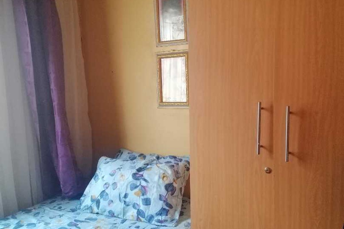 A compact bedroom featuring built-in wooden cabinetry and a window with curtains, offering functional storage space.