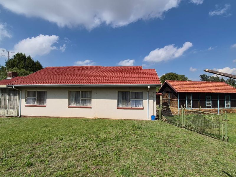 Rear view of the property featuring a tiled roof, plastered exterior walls, and an adjacent outbuilding set within a spacious garden area.