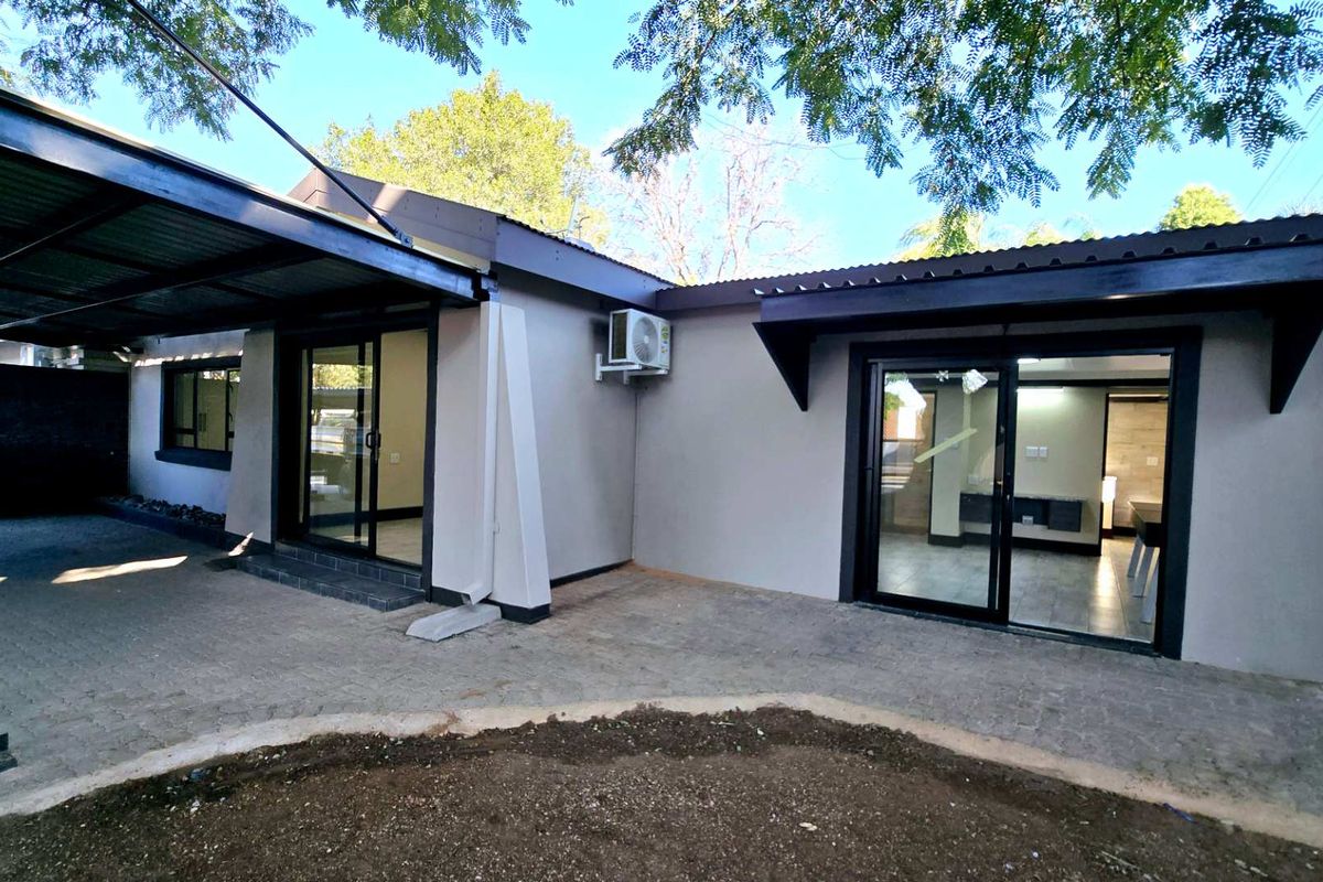 Rear exterior view of the townhouse featuring a paved patio area, covered carport, and sliding glass door access to the interior living spaces.