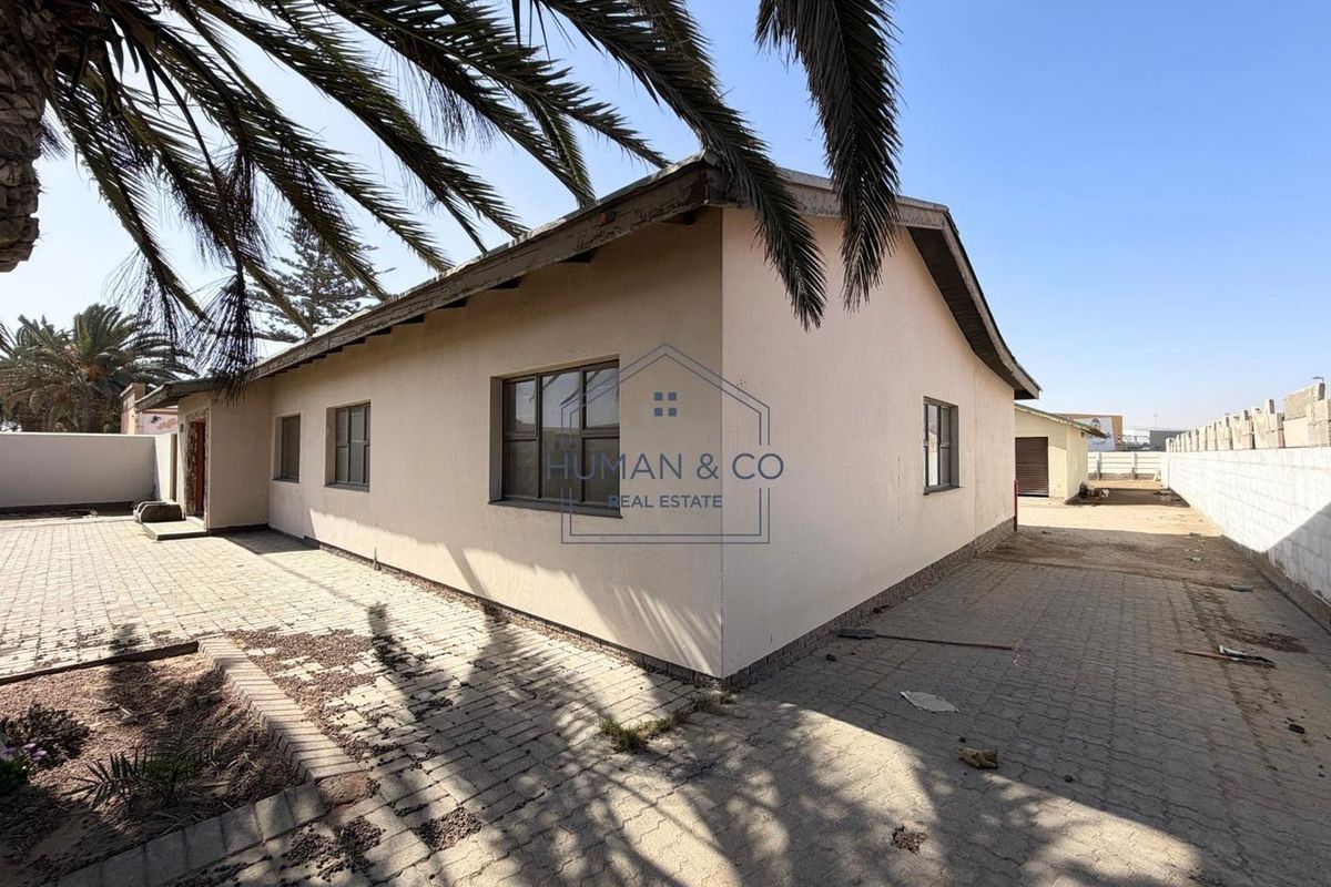 Rear view of the property featuring a paved yard, boundary wall, and exterior building facade with aluminum window frames.
