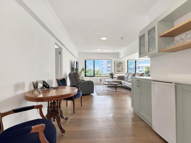 Spacious open-plan living area featuring hardwood flooring, crown molding, recessed lighting, and a modern built-in kitchenette with cabinetry.