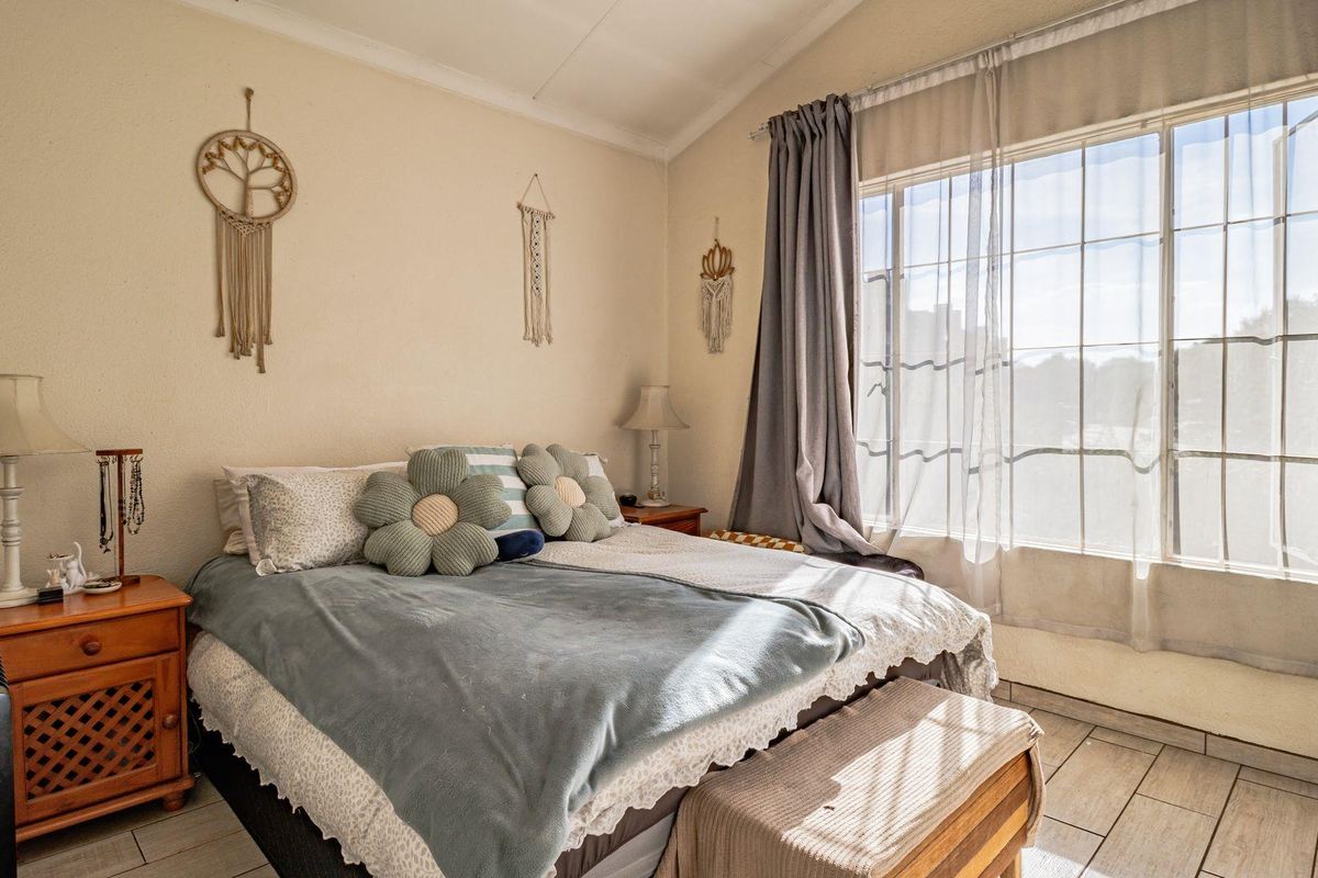 A bright bedroom featuring tiled flooring, a large window with natural light, and a vaulted ceiling.
