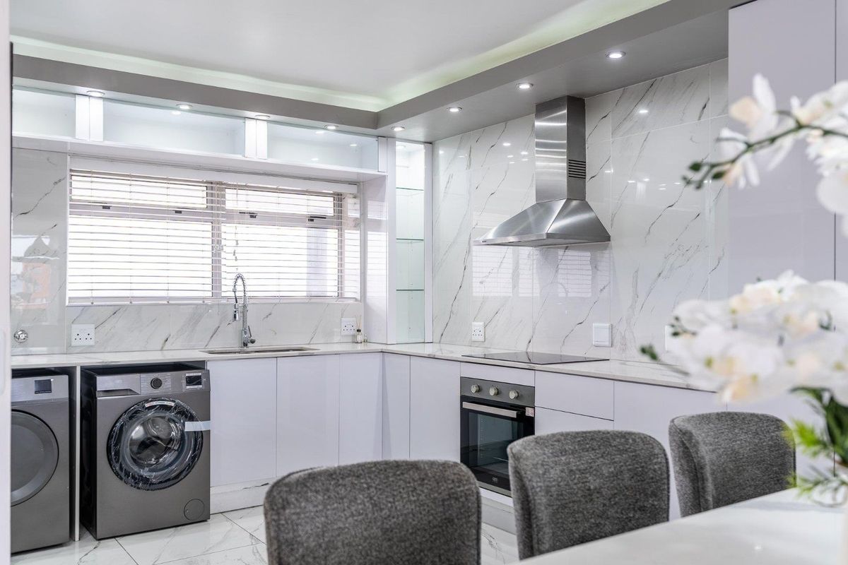 Modern kitchen featuring marble-look wall tiles, integrated cabinetry, stainless steel appliances, and recessed lighting, offering a sleek and functional culinary space.
