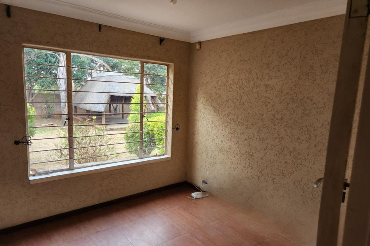 A vacant bedroom featuring textured walls, tiled flooring, and large windows with security bars overlooking the garden.