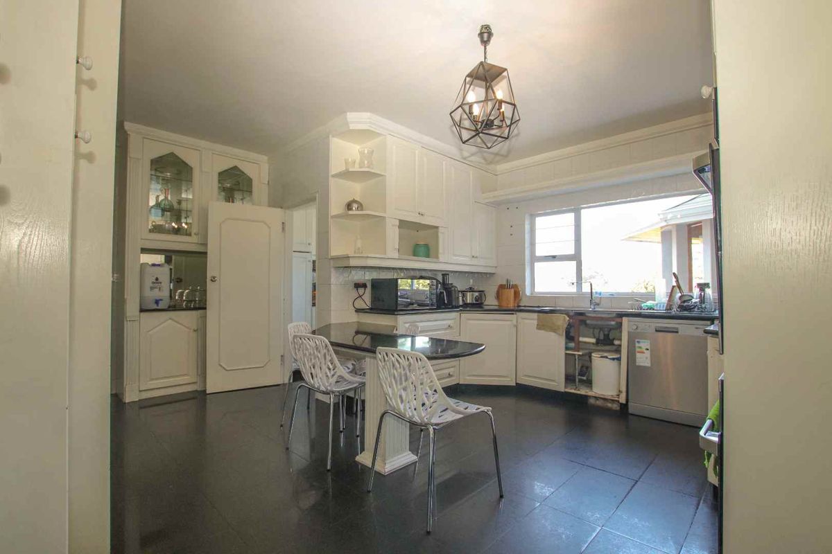A functional kitchen featuring white cabinetry, dark countertops, a central breakfast bar, and a large window providing natural light.