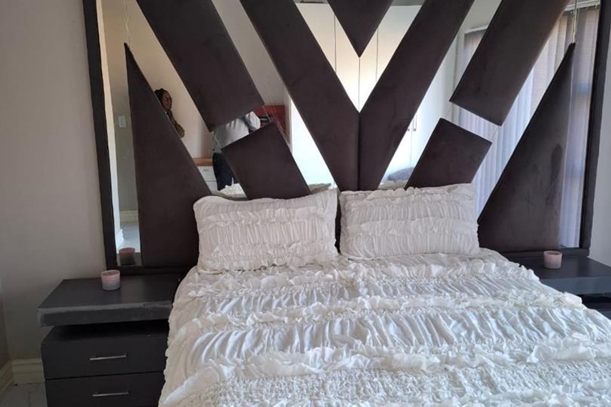 A bedroom featuring a large, custom-designed geometric headboard with integrated mirror panels and built-in bedside cabinetry.