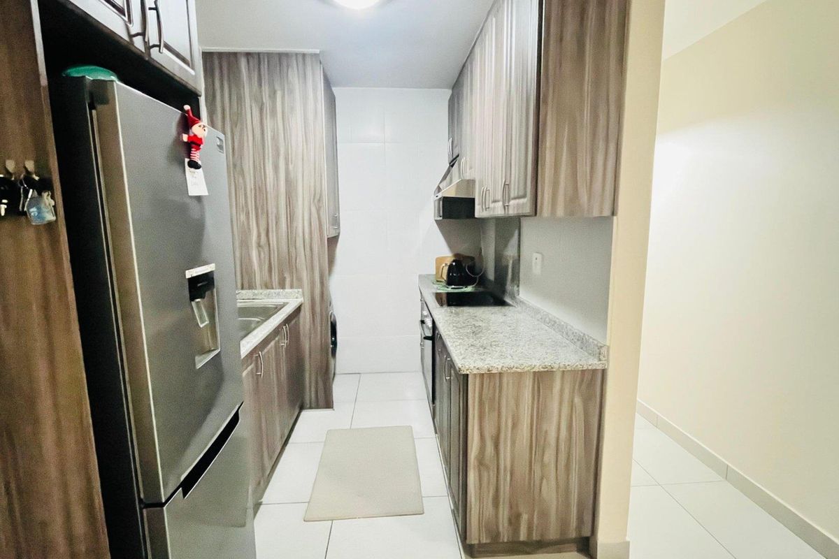 A galley-style kitchen featuring wood-grain cabinetry, granite countertops, and integrated appliances, offering a functional and modern workspace.