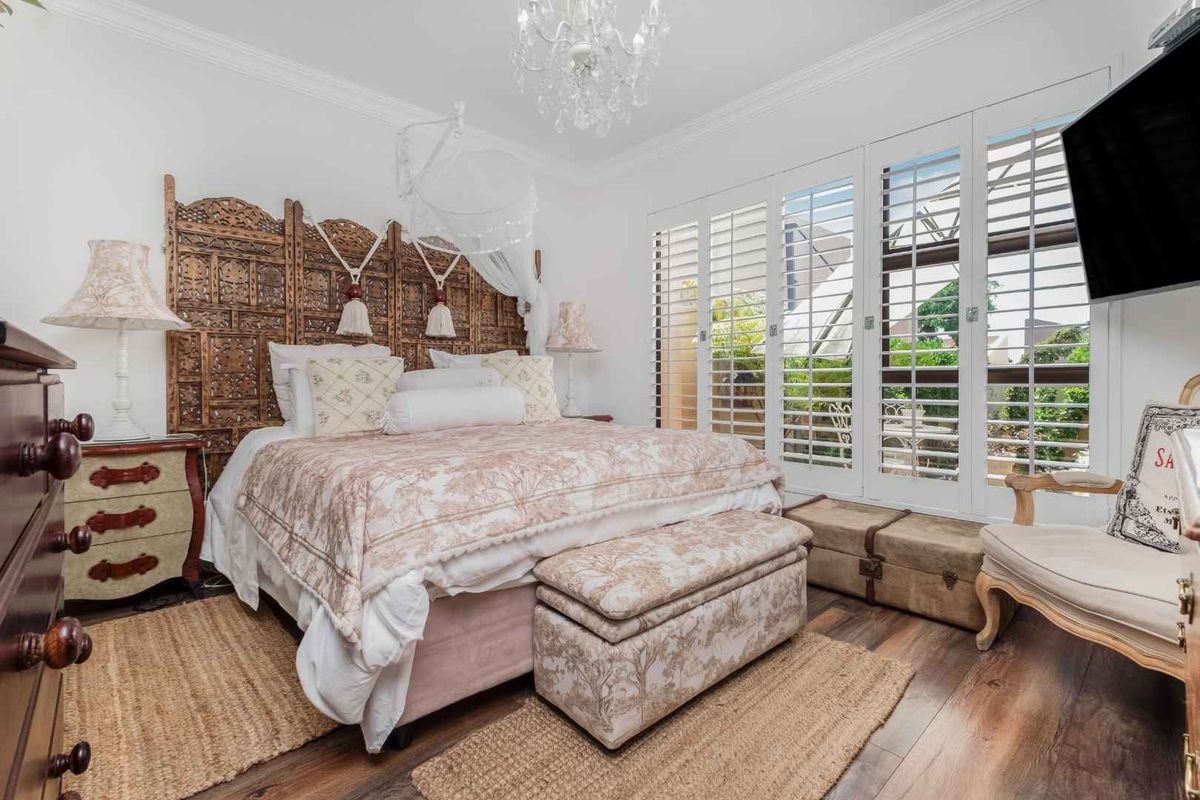 A well-maintained bedroom featuring timber-look flooring, crown molding, and white plantation shutters opening to an outdoor area.