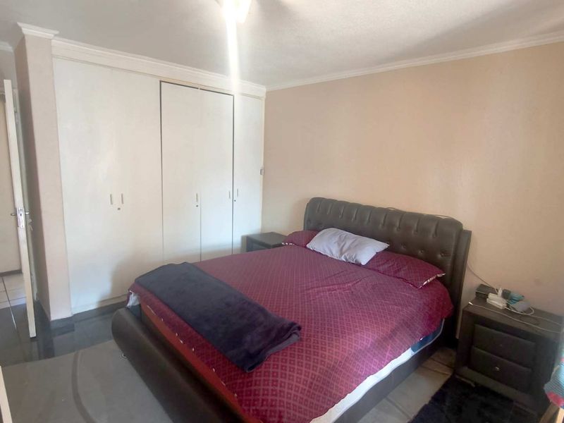 A standard bedroom featuring built-in cupboards, tiled flooring, and decorative coving, offering a functional space with neutral wall finishes.