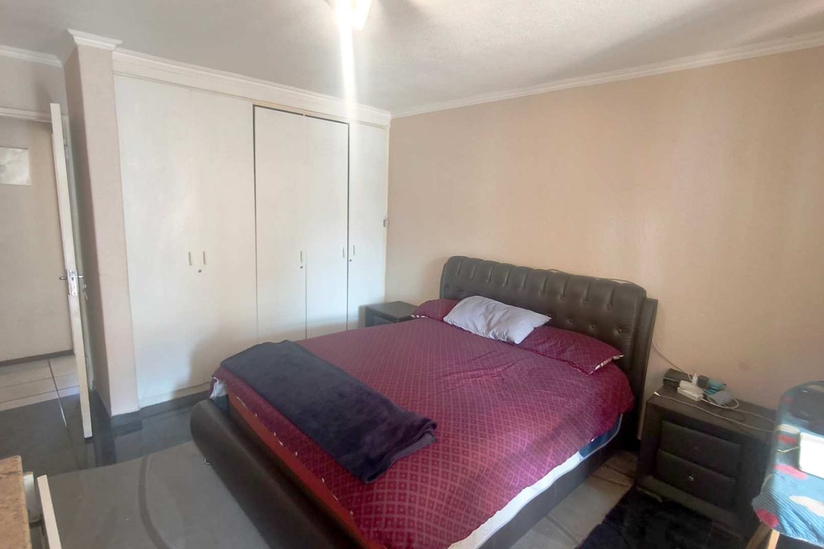 A standard bedroom featuring built-in cupboards, tiled flooring, and decorative coving, offering a functional space with neutral wall finishes.
