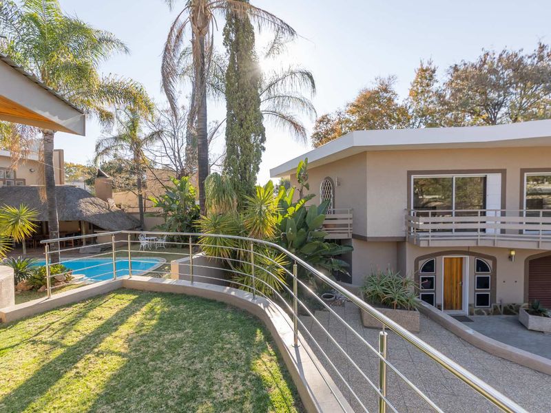 Rear exterior view featuring a swimming pool, a thatched lapa, a raised lawn area with stainless steel balustrades, and a multi-level residential structure.
