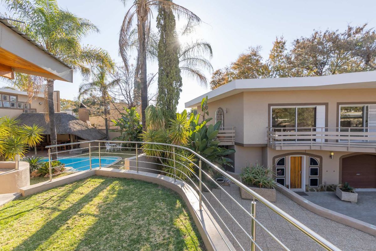 Rear exterior view featuring a swimming pool, a thatched lapa, a raised lawn area with stainless steel balustrades, and a multi-level residential structure.