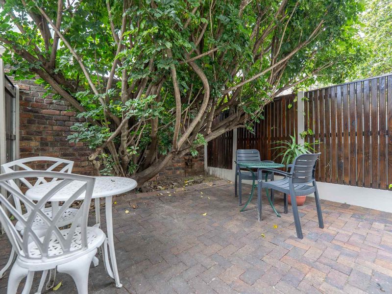 A private rear courtyard featuring brick paving, enclosed by a combination of brick and timber slat fencing with mature tree coverage.