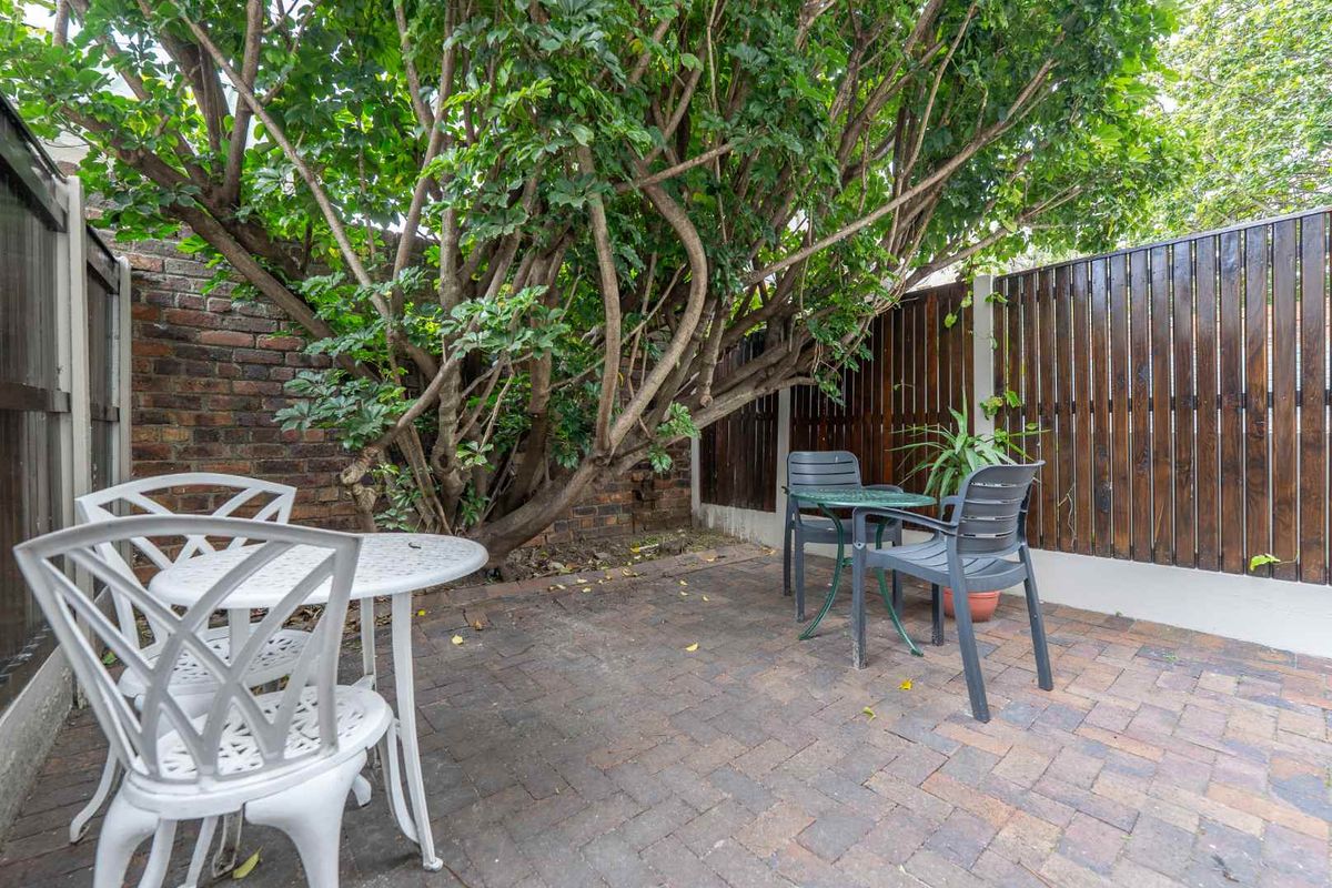A private rear courtyard featuring brick paving, enclosed by a combination of brick and timber slat fencing with mature tree coverage.