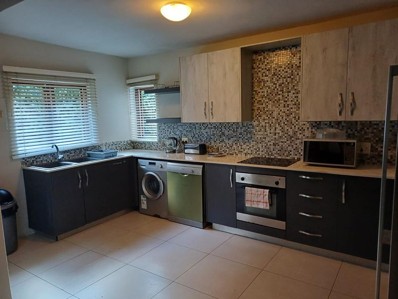 A functional kitchen featuring dark lower cabinetry, light upper cabinets, a mosaic tile backsplash, integrated oven, hob, and tiled flooring.