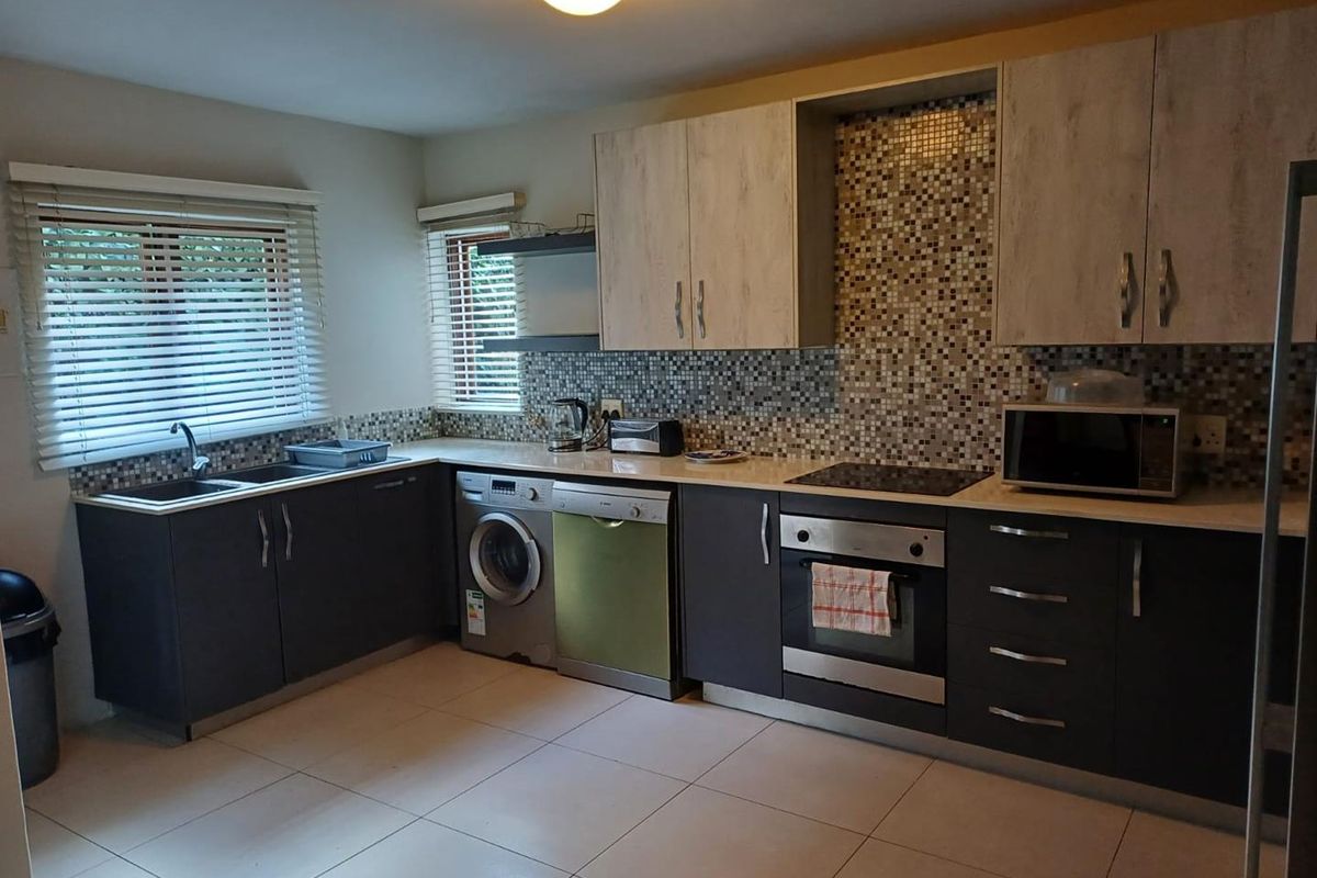 A functional kitchen featuring dark lower cabinetry, light upper cabinets, a mosaic tile backsplash, integrated oven, hob, and tiled flooring.