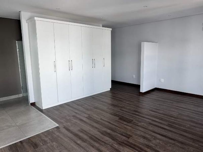 Spacious bedroom featuring modern laminate flooring, neutral walls, and extensive built-in cupboard storage.