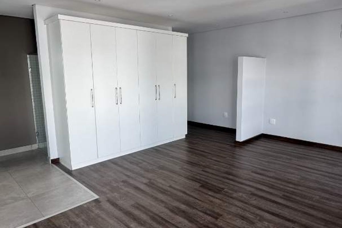 Spacious bedroom featuring modern laminate flooring, neutral walls, and extensive built-in cupboard storage.