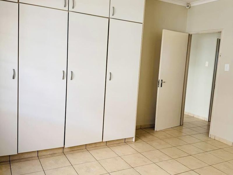 A vacant bedroom featuring floor-to-ceiling built-in cupboards, neutral tiled flooring, and a coved ceiling, offering a clean and functional space.