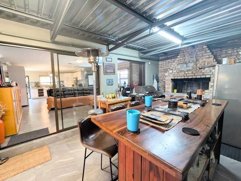 Covered patio area featuring a built-in brick fireplace, exposed steel roof beams, and large sliding glass doors providing access to the interior living space.