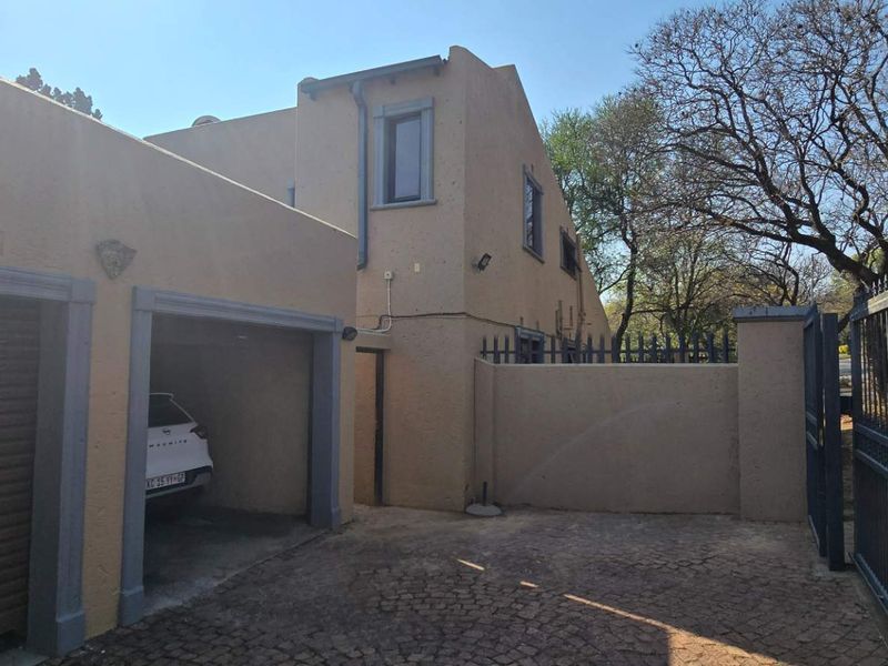 Front exterior view of the property featuring a paved driveway, garage access, and secure perimeter wall with metal gate.