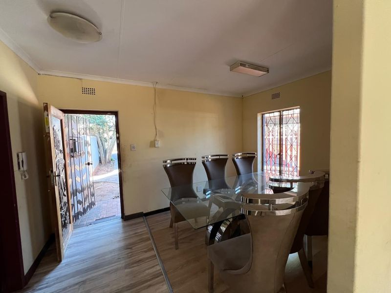 Dining area featuring laminate flooring, security gate access, and burglar bars on windows. The space requires cosmetic updates to improve its overall condition.