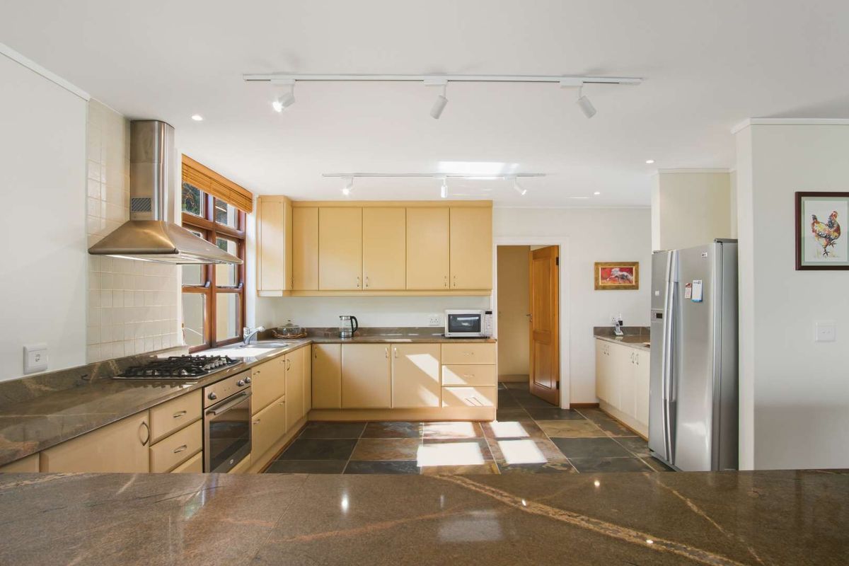A functional kitchen featuring granite countertops, gas hob, built-in oven, stainless steel extractor fan, and slate tile flooring with ample cabinetry.