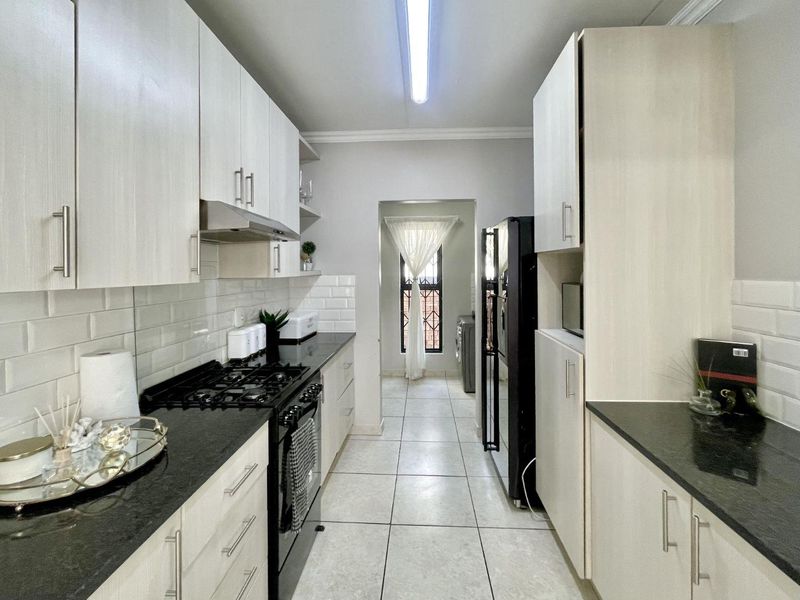 A well-maintained galley kitchen featuring light wood cabinetry, dark granite countertops, subway tile backsplash, and a gas hob with an integrated extractor fan.