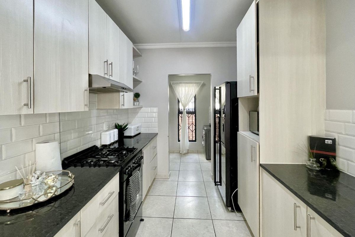 A well-maintained galley kitchen featuring light wood cabinetry, dark granite countertops, subway tile backsplash, and a gas hob with an integrated extractor fan.